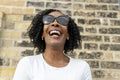 Portrait of woman in sunglasses laughing against brick wall