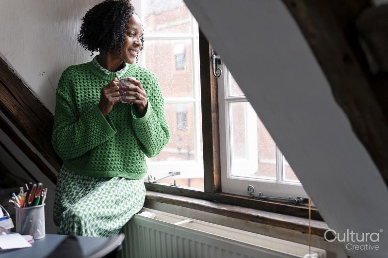 Smiling businesswoman holding cup of coffee while looking through window