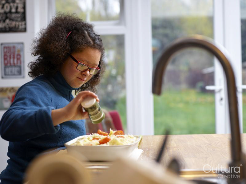 Girl with Down Syndrome seasoning dish in kitchen
