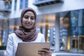 Smiling businesswoman in hijab using digital tablet in city