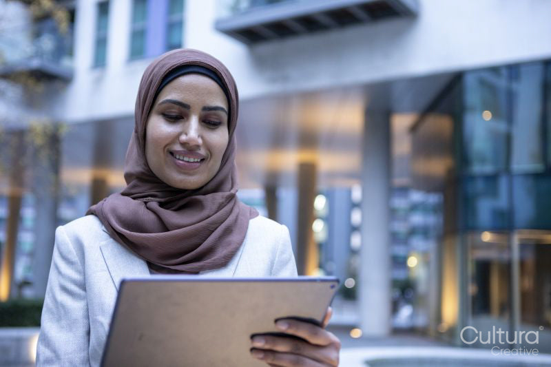 Smiling businesswoman in hijab using digital tablet in city