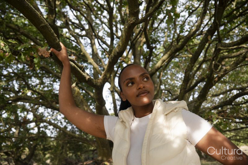Portrait of young woman standing under tree, reaching to branch