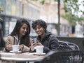 Smiling female couple using phone in sidewalk cafe