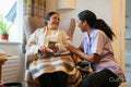 Senior lady sitting in armchair and showing phone to nurse at nursing home