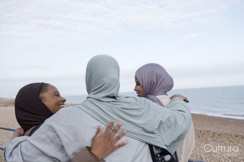 Three Muslim friends embracing on beach