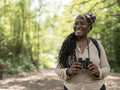 Smiling female hiker holding binoculars in forest