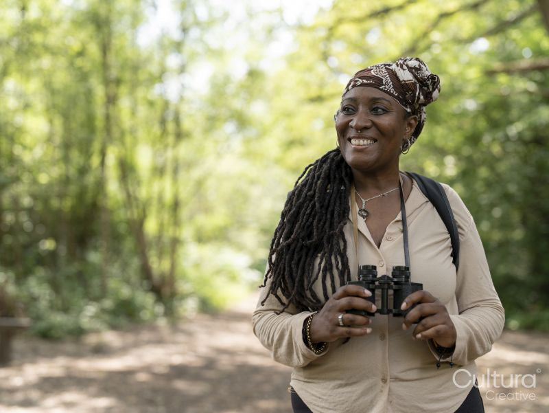 Smiling female hiker holding binoculars in forest