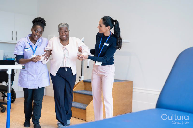 Female therapist and nurse supporting senior woman walking in exercise room
