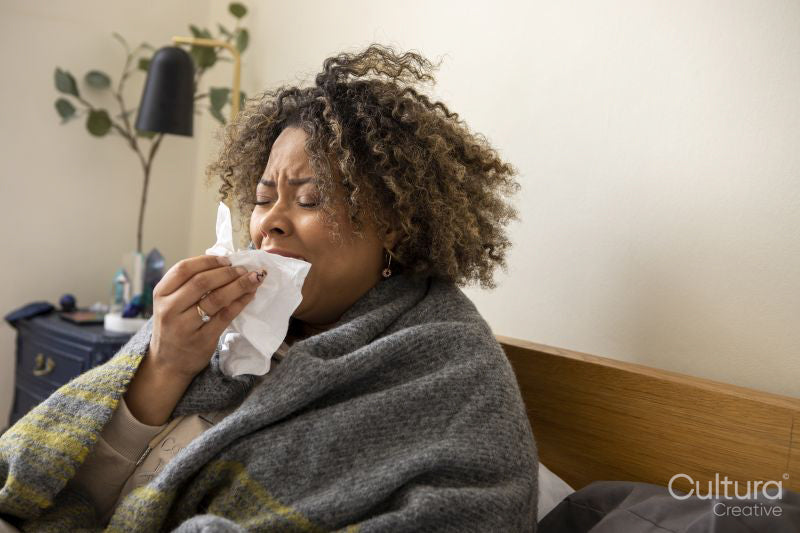 Woman wrapped in blanket sneezing