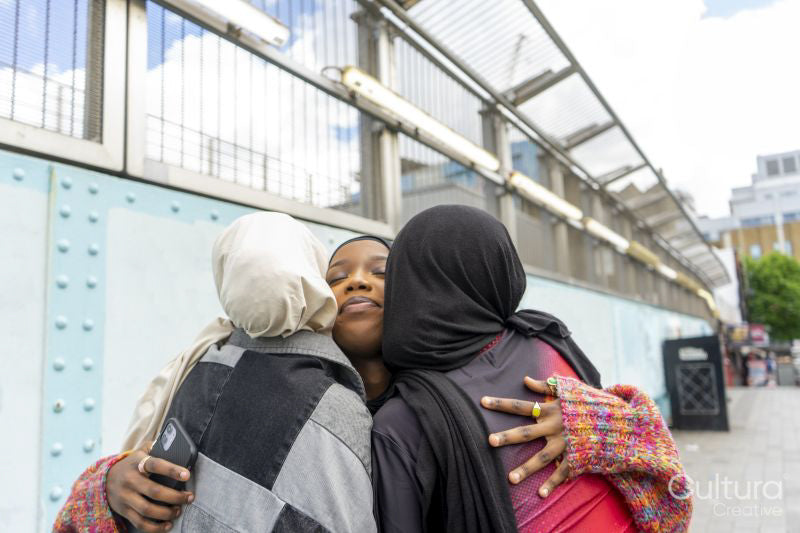 Young women wearing hijabs hugging in city