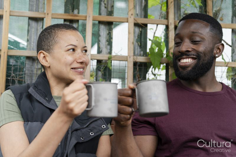 Smiling couple with metal mugs relaxing in urban garden