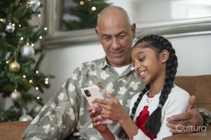 Senior man with granddaughter looking at smart phone at Christmas tree