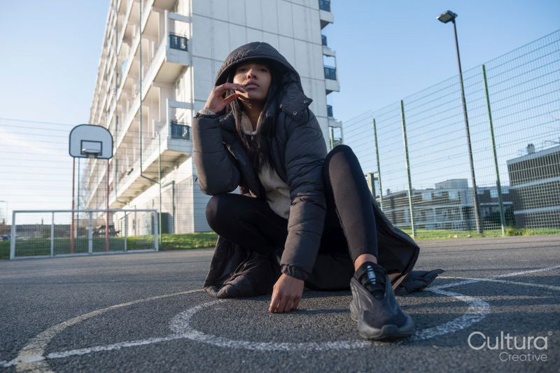 Portrait of woman in overcoat with hood sitting on basketball court