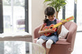Little girl playing on ukulele in living room