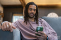 Man with dreads relaxing on sofa and using phone