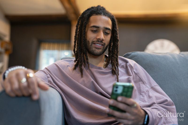 Man with dreads relaxing on sofa and using phone