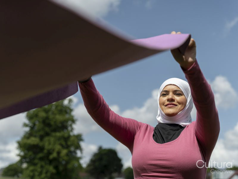 Sutton,Woman in headscarf unrolling yoga mat outdoors