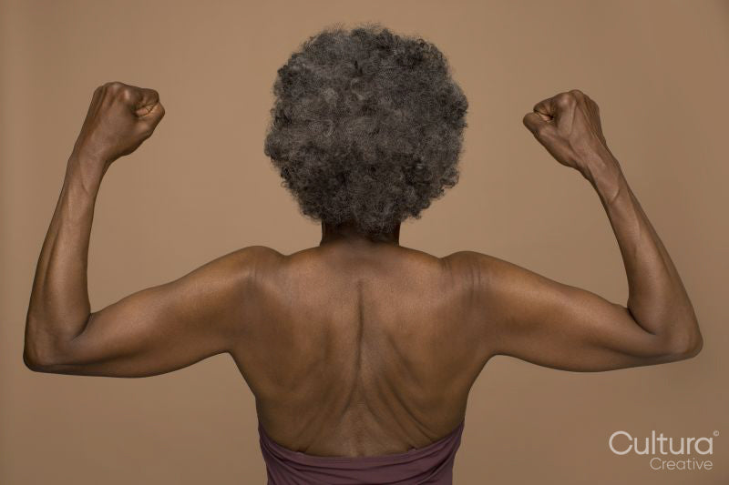 Rear view of shirtless senior woman flexing muscles