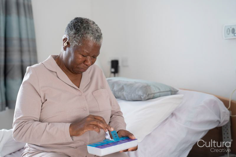 Senior woman in pajamas sitting on bed, holding pill organizer