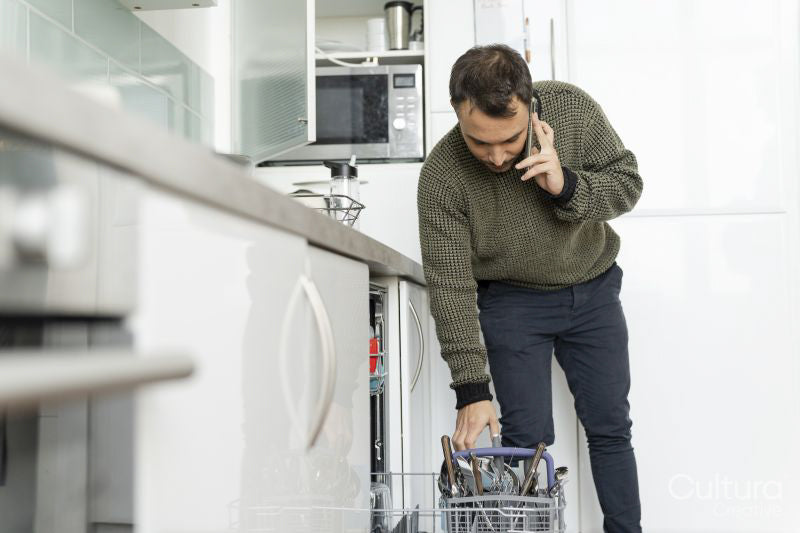 Mature man unloading dishwasher and talking on phone