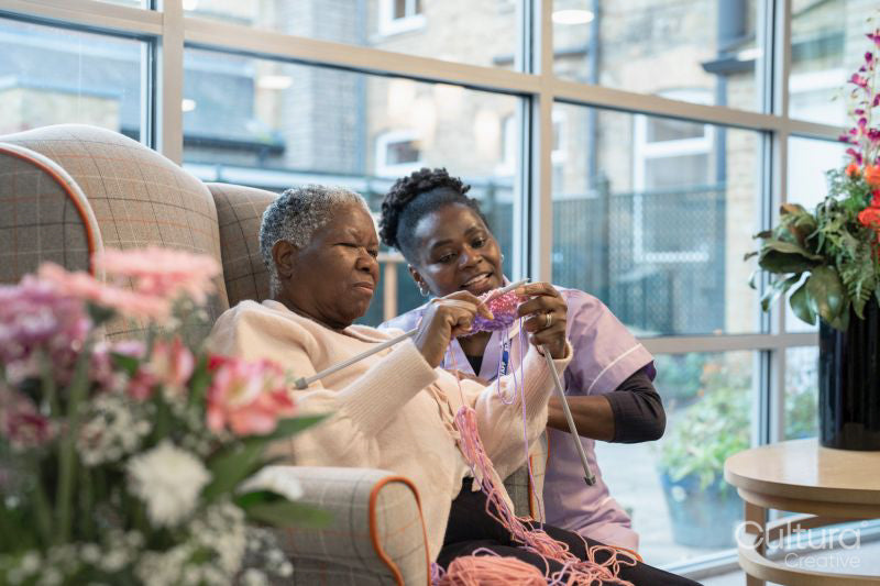 Smiling nurse looking at senior woman knitting in nursing home