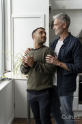 Mature male couple standing by window at home