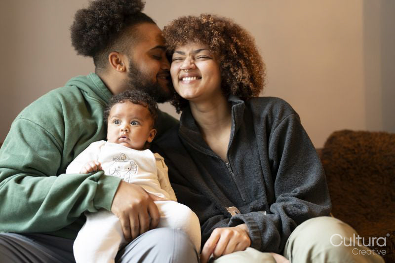 Happy parents sitting on sofa with baby daughter