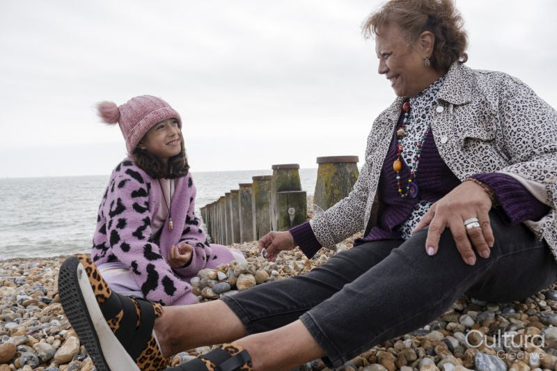 Grandmother and granddaughter sitting on beach on cloudy day