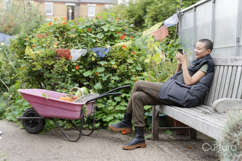 Smiling woman with smart phone in vegetable garden