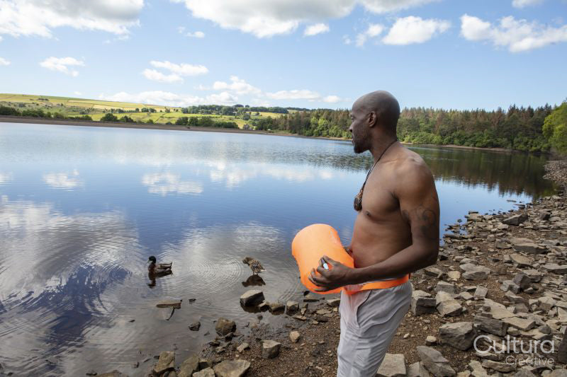 Shirtless man with buoy standing on rocky lakeshore, Yorkshire, UK