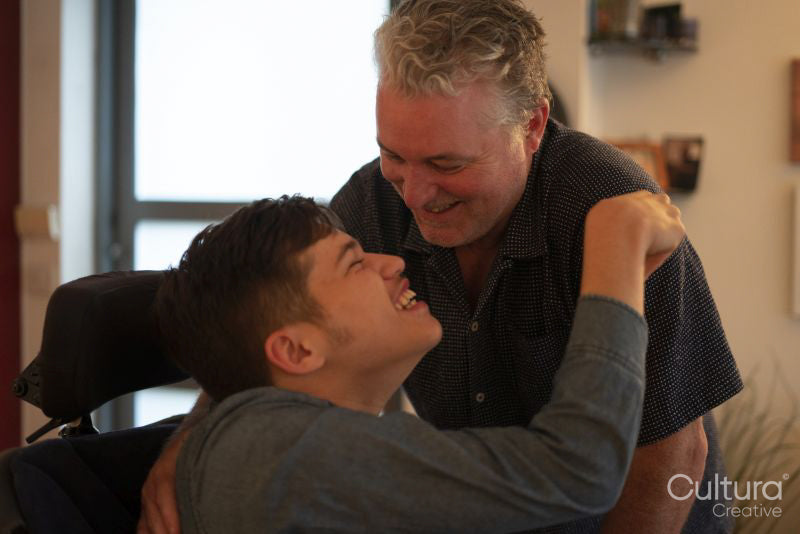 Father embracing disabled son at home