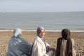 Three Muslim women sitting on beach on sunny day