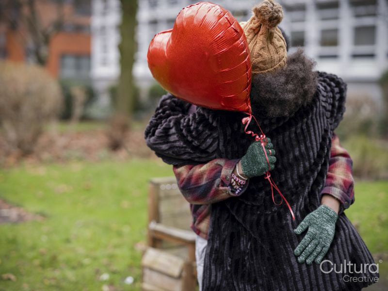 Couple with red heart shaped balloon hugging outdoors
