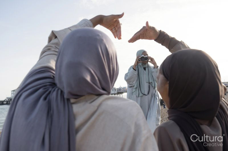 Woman photographing Muslim friends making heart shape with hands on beach