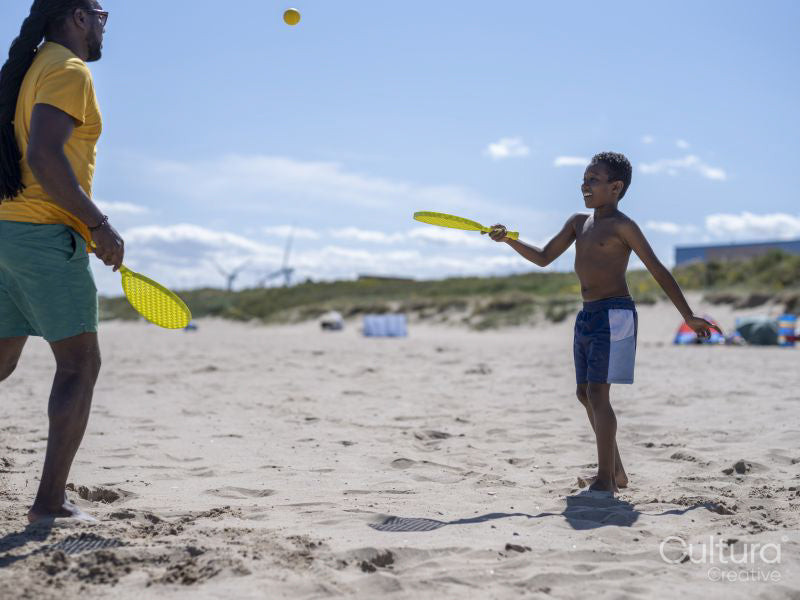 Father and son playing padel on beach
