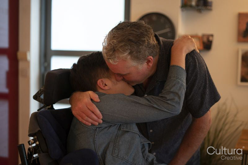 Father embracing disabled son at home