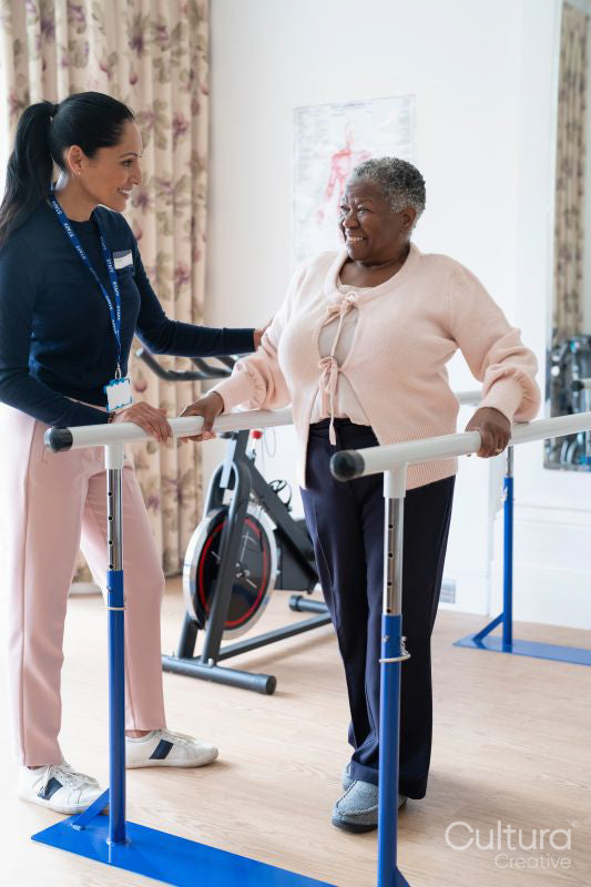 Smiling female therapist assisting senior woman walking on bars