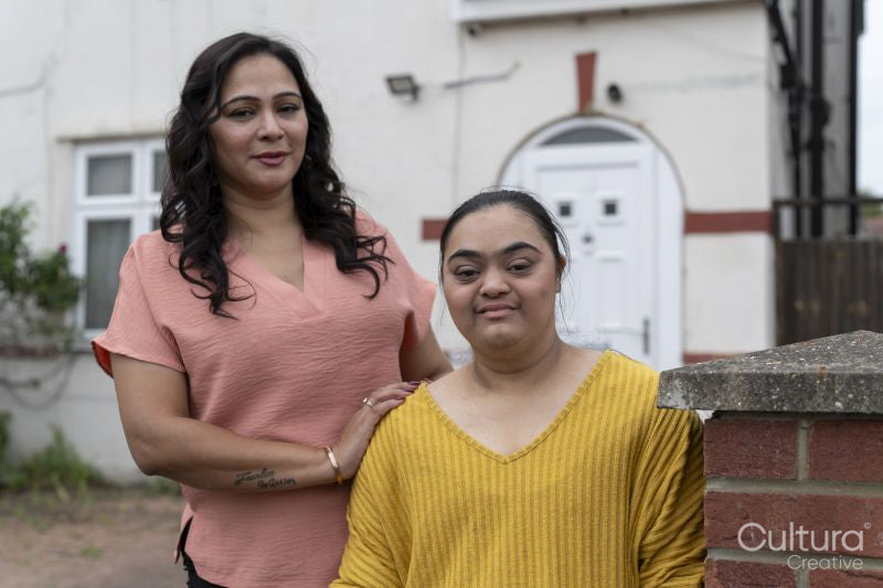 Portrait of woman with down syndrome daughter standing in front of house
