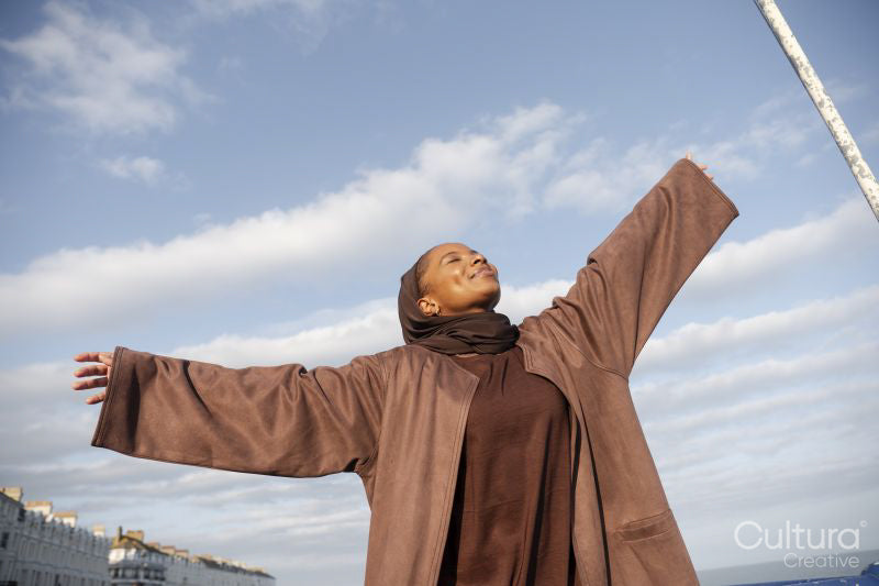 Portrait of smiling Muslim woman standing with arms outstretched