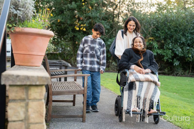 Family during walk outside nursing home with senior lady sitting in wheelchair