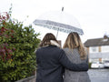 Back view of two women wearing coats under umbrella in rain