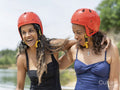 Smiling women wearing sports helmets by lake