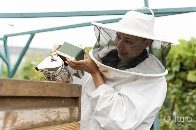 Female beekeeper using smoker in urban garden