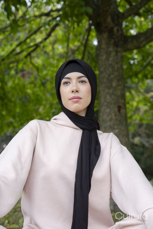 Portrait of woman in hijab and pink tracksuit sitting in park