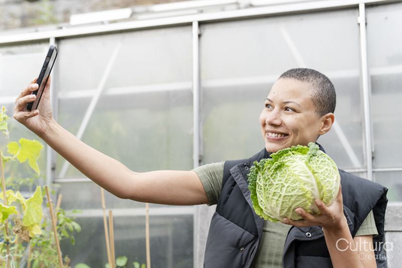 Smiling woman taking selfie with homegrown cabbage in allotment