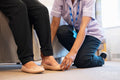 Nurse helping senior lady to put on her shoes at nursing home