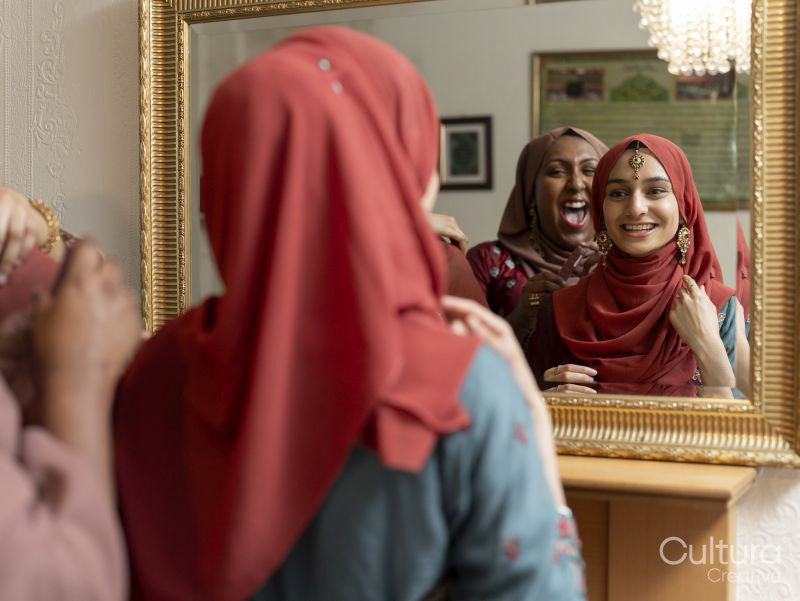 Smiling women preparing for Ramadan celebration in front of mirror at home