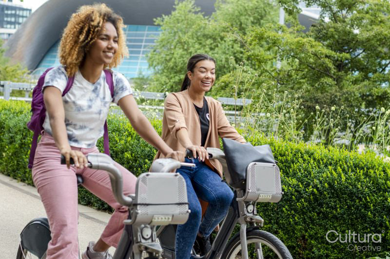 Two smiling women cycling together in city