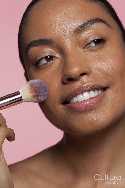 Studio portrait of smiling beautiful woman using powder brush