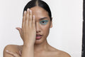 Woman wearing blue makeup, shielding part of face with hand